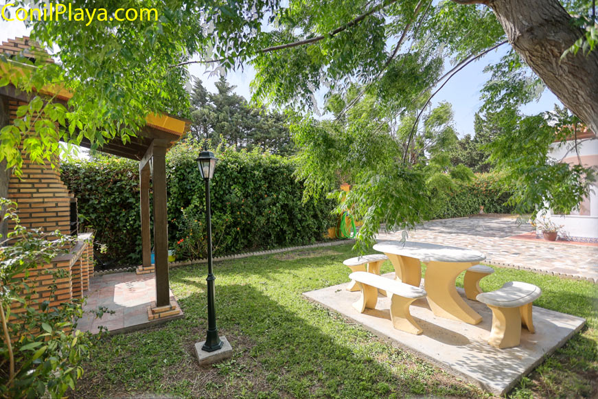 Zona ajardinada con barbacoa cubierta y mesa de exterior visible en primer plano