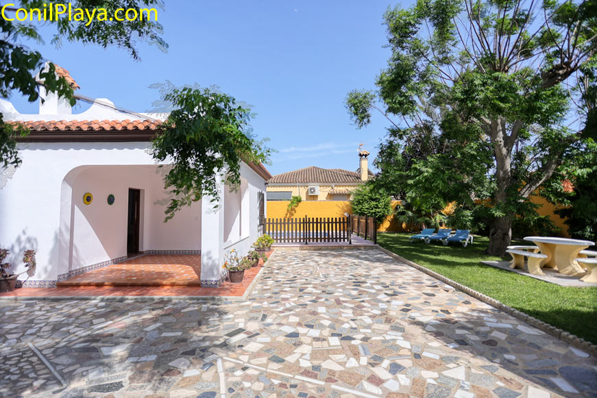 Jardín con seto, mesa exterior y acceso junto fachada de una casa blanca