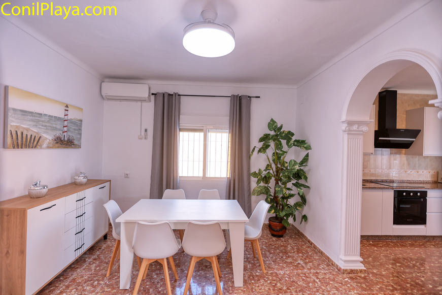 Comedor moderno con mesa blanca y seis sillas junto a ventana y cocina abierta