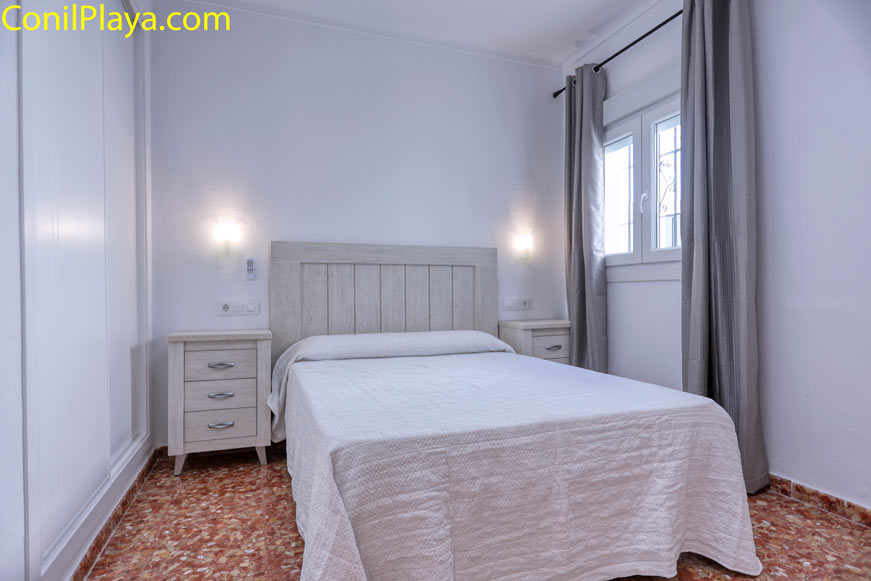 Dormitorio con cama doble, dos mesitas, armario y ventana lateral