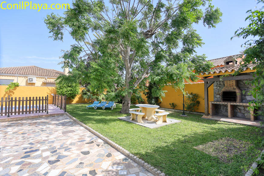Vista de jardín con barbacoa, mesa de picnic, piscina y tumbonas junto a vivienda