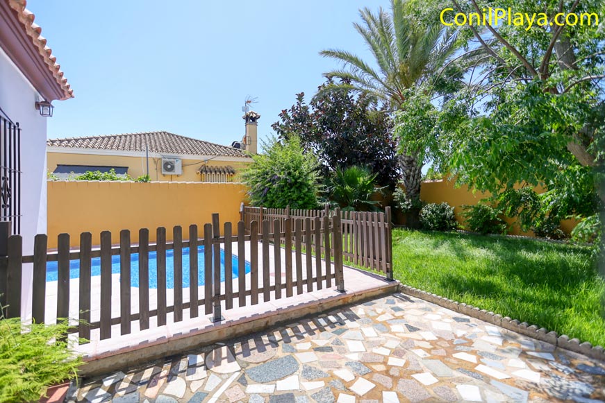 Piscina vallada junto a la casa y jardín con césped visible en primer plano