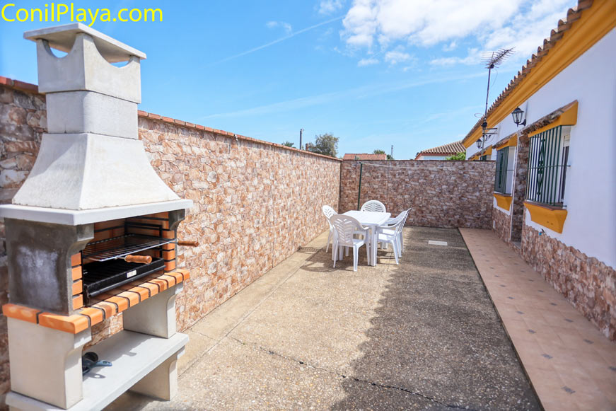 Patio exterior con barbacoa de obra y mesa con sillas de plástico blancas