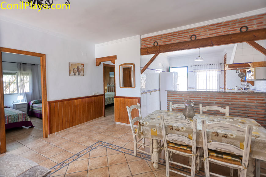 Comedor luminoso con mesa de madera junto a cocina abierta y acceso a dormitorios