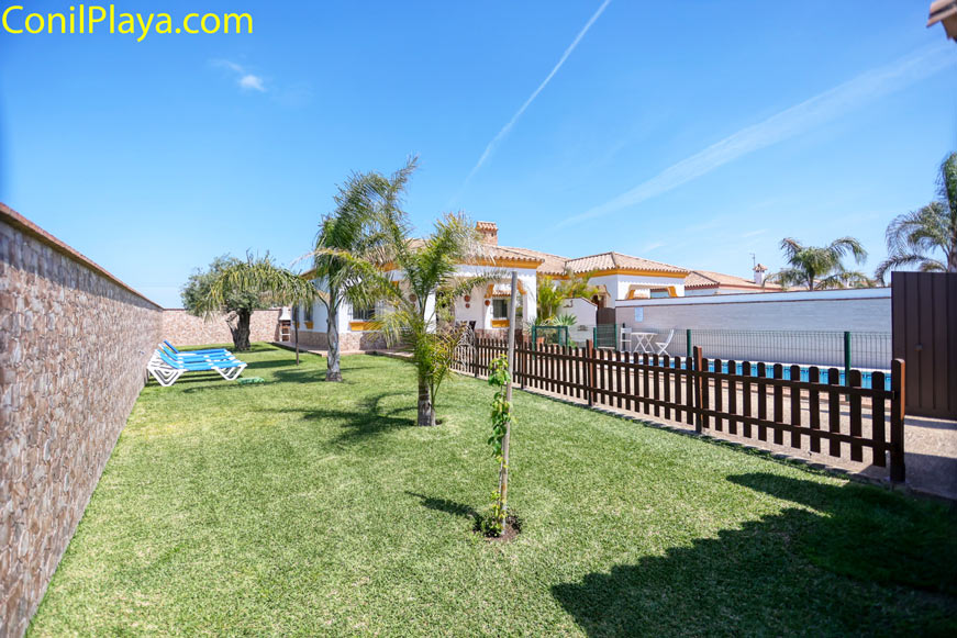 Jardín con césped, árboles, tumbonas y zona vallada junto a vivienda