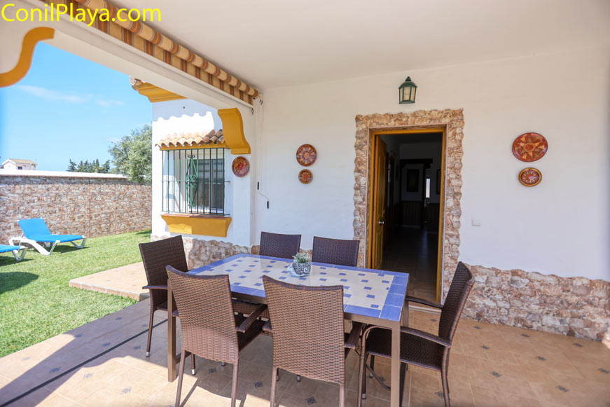 Mesa de comedor exterior en porche junto a pared decorada y jardín césped