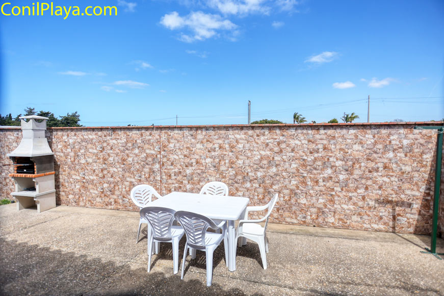 Patio con mesa de plástico blanca y barbacoa junto a muro de ladrillo