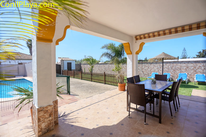 Zona de porche con mesa y sillas junto piscina y jardín privado