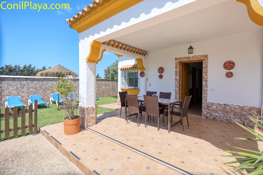 Porche amueblado con mesa y sillas junto a jardín y tumbonas