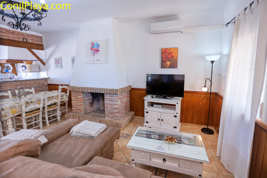 salón con chimenea aire acondicionado sofá mesa y televisión decorado en tonos claros