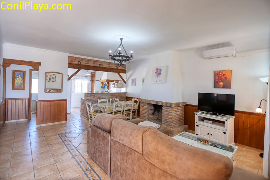 Salón luminoso con chimenea, sofá grande, mesa de comedor y cocina abierta