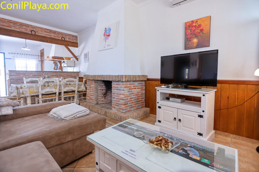 Salón luminoso con sofá, chimenea de ladrillo y televisión sobre mueble blanco