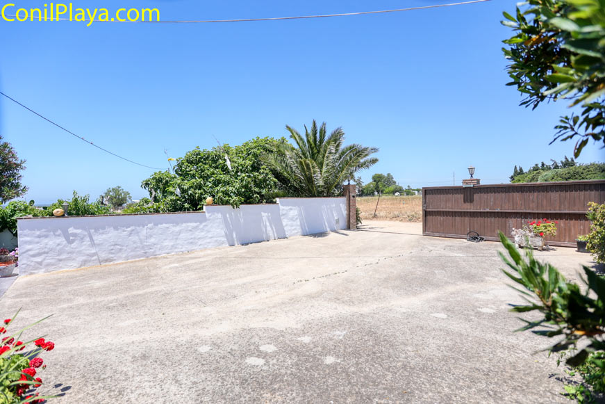 Aparcamiento amplio pavimentado junto a muro blanco y portón de madera