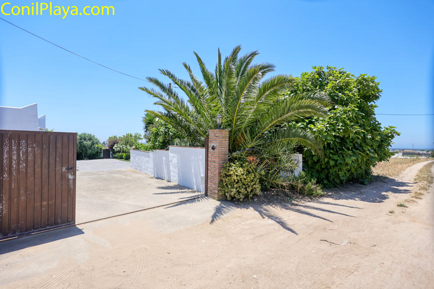 Entrada exterior con portón metálico y vegetación junto a carril de acceso