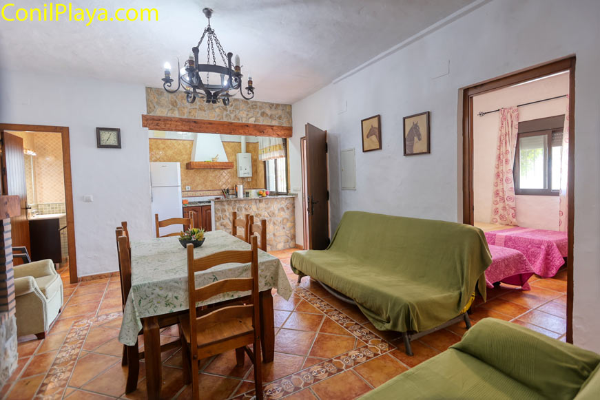 Salón con mesa de comedor, sofá y cocina al fondo vistos desde la entrada