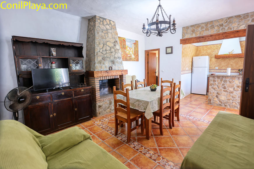 Salón rústico con chimenea, mesa de comedor y cocina abierta al fondo
