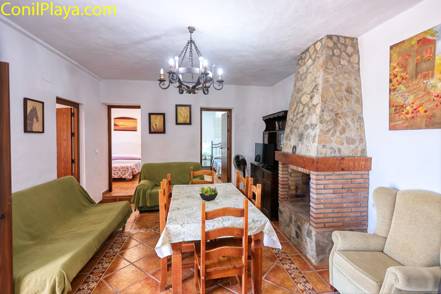 Salón con chimenea rústica, mesa comedor y sofás vistos desde la entrada