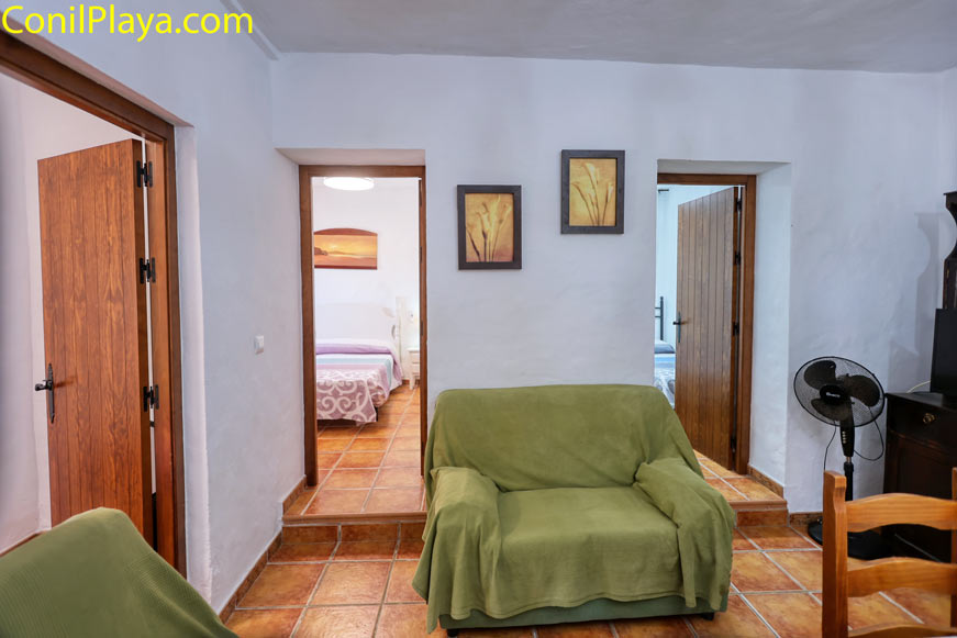 Salón con sofá verde y acceso a dos dormitorios con paredes blancas