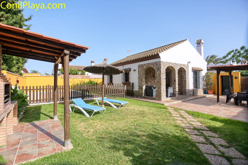 Jardín con césped, sombrilla, tumbonas y zona de barbacoa