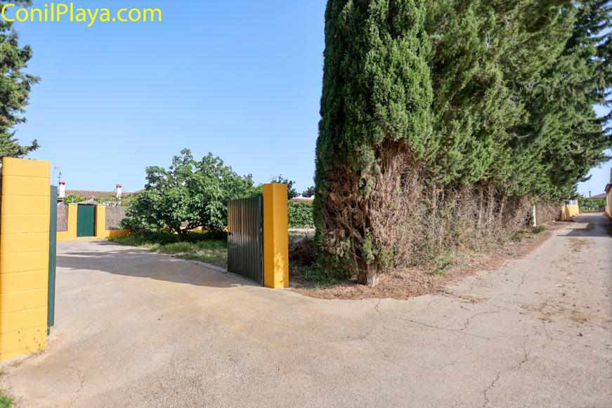 Entrada visible con portón abierto y árboles junto a la zona de aparcamiento