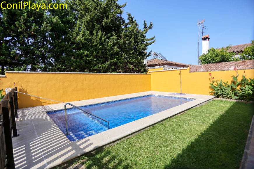 Piscina privada rectangular rodeada de césped y pared amarilla desde el acceso