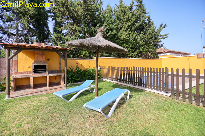 Zona de piscina vallada con tumbonas y barbacoa de obra en jardín privado