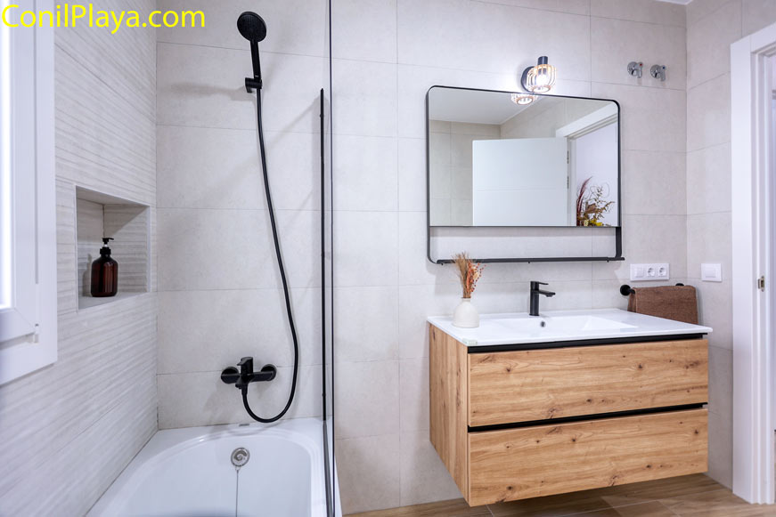 Cuarto de baño moderno con bañera grifería negra y mueble madera