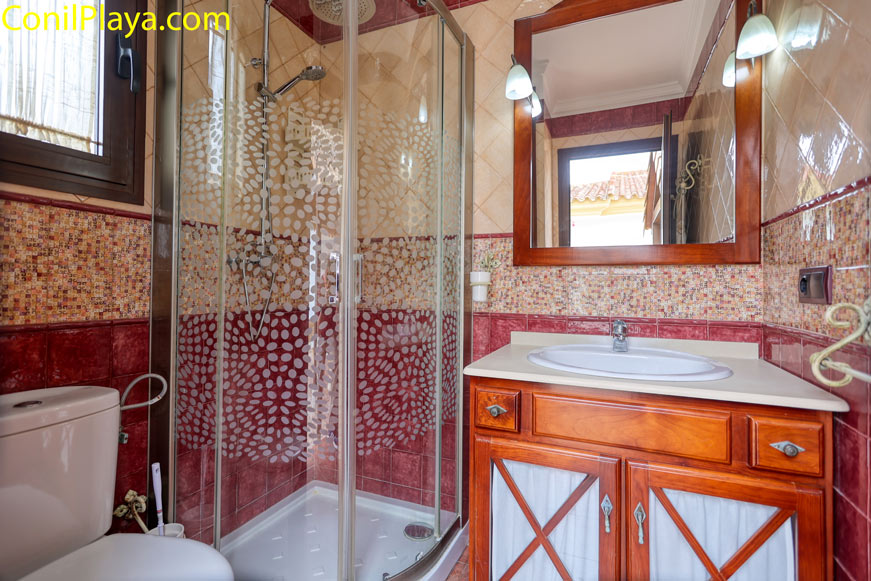 Cuarto de baño con ducha de mampara y lavabo de madera visto desde la entrada