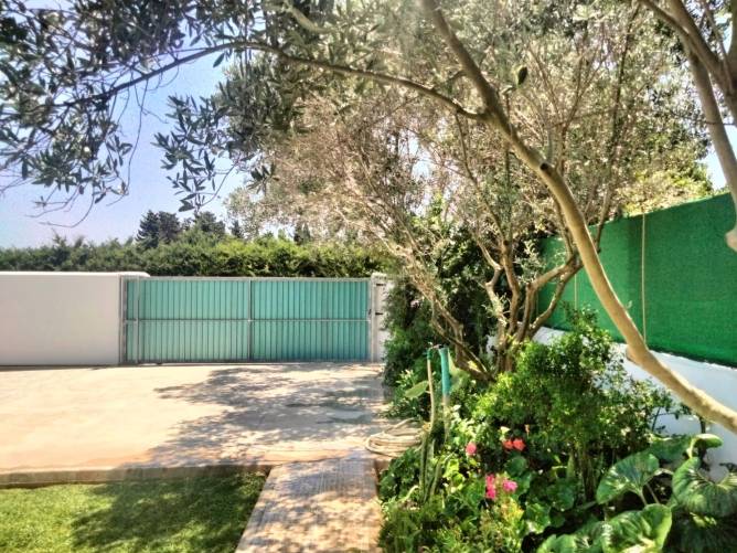 Aparcamiento exterior junto a portón metálico y jardín con plantas verdes