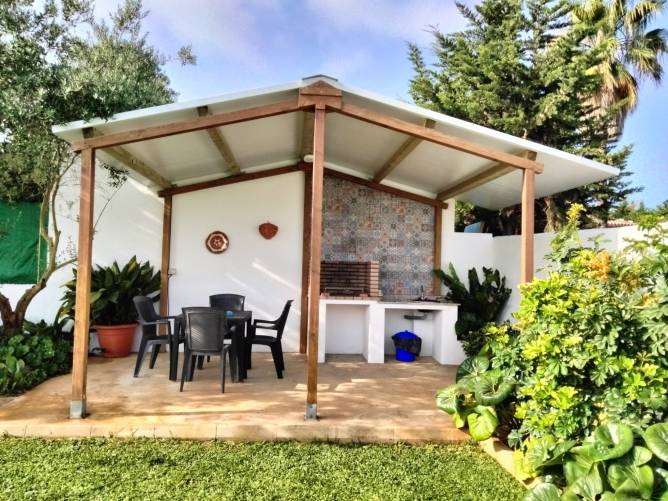 Barbacoa techada con mesa y sillas en jardín de chalet en alquiler