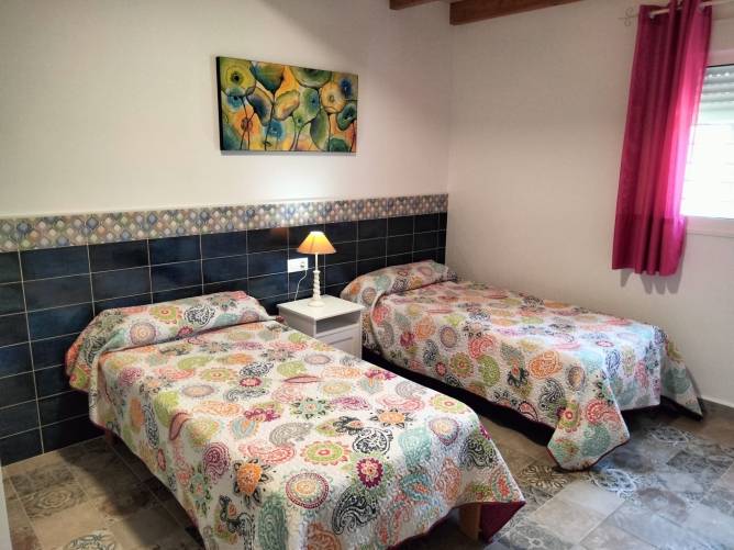 Dormitorio con dos camas individuales, colchas coloridas y ventana con cortina rosa