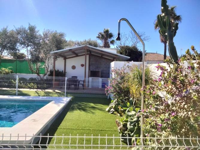 Piscina vallada con ducha exterior y barbacoa techada en jardín soleado
