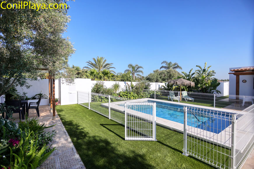 Piscina vallada junto a jardín privado y zona de sombra con mesa y sillas