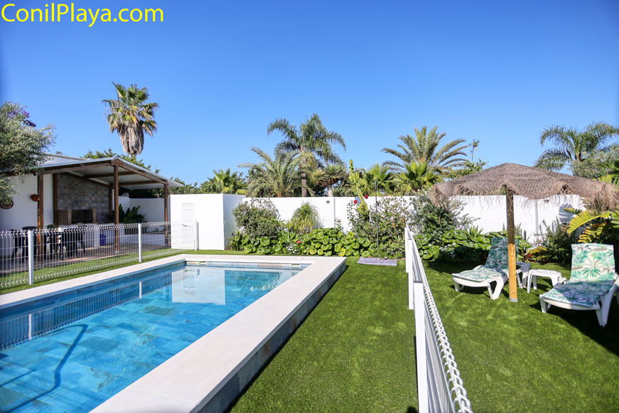 Piscina vallada junto a zona de césped artificial y dos tumbonas con sombrilla