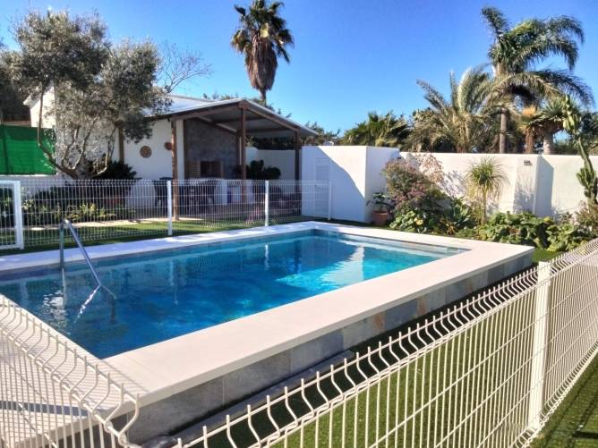 La piscina está vallada con una malla metálica, al fondo se encuentra la barbacoa techada