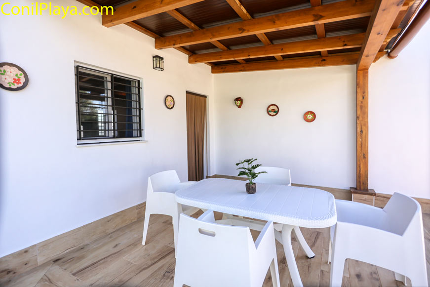 Porche cubierto con mesa blanca y cuatro sillas en pared decorada