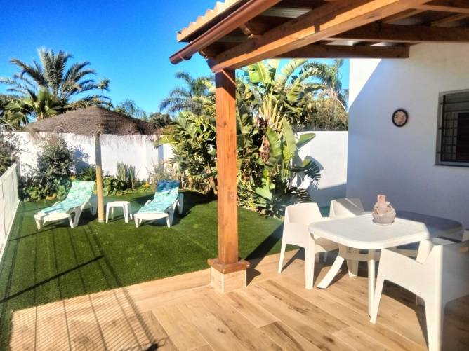 Porche con mesa, sillas, tumbonas y jardín tropical en alojamiento vacacional