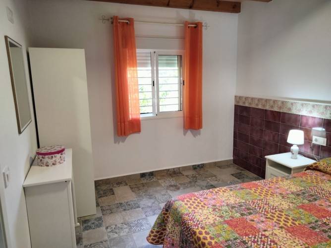 Dormitorio luminoso con ventana, cortinas naranjas y cama colorida.