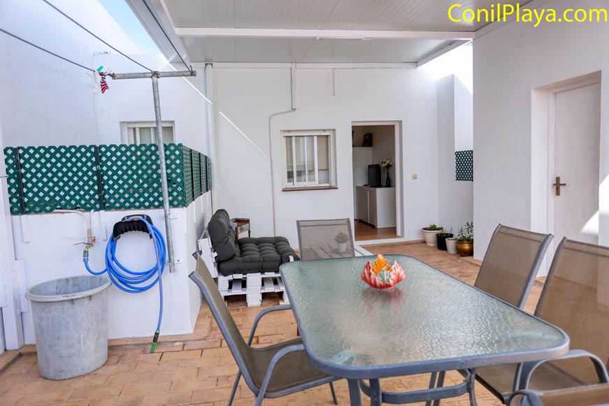 Terraza cubierta con mesa de cristal y sillas junto a entrada de la casa