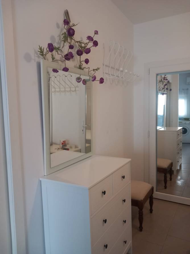 Cómoda blanca con espejo y flores decorativas junto a una silla
