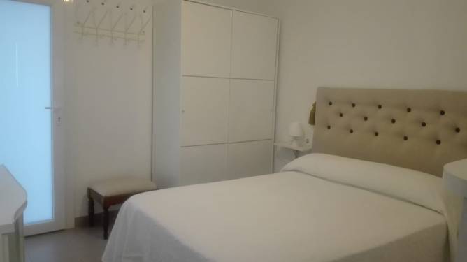 Dormitorio con cama grande, armario y mesilla blanca junto a la puerta