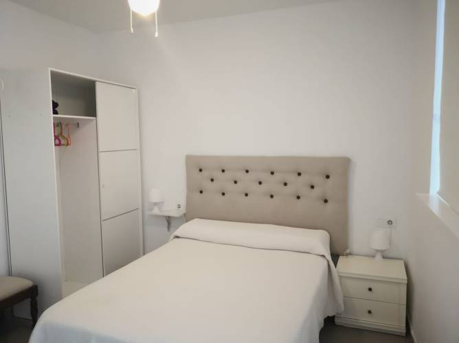 Dormitorio con cama de matrimonio, armario blanco y mesitas, vista desde la entrada