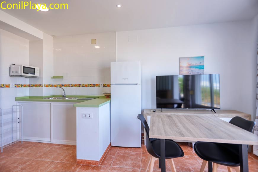 Cocina moderna junto a comedor con mesa, sillas y televisión