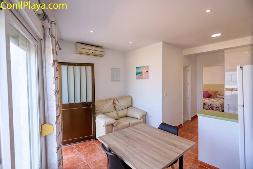 Salón con sofá beige y mesa, vista parcial de dormitorio