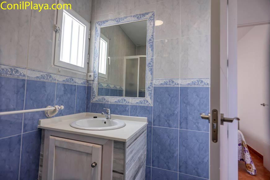 Lavabo blanco con espejo grande y ventana en cuarto de baño azul