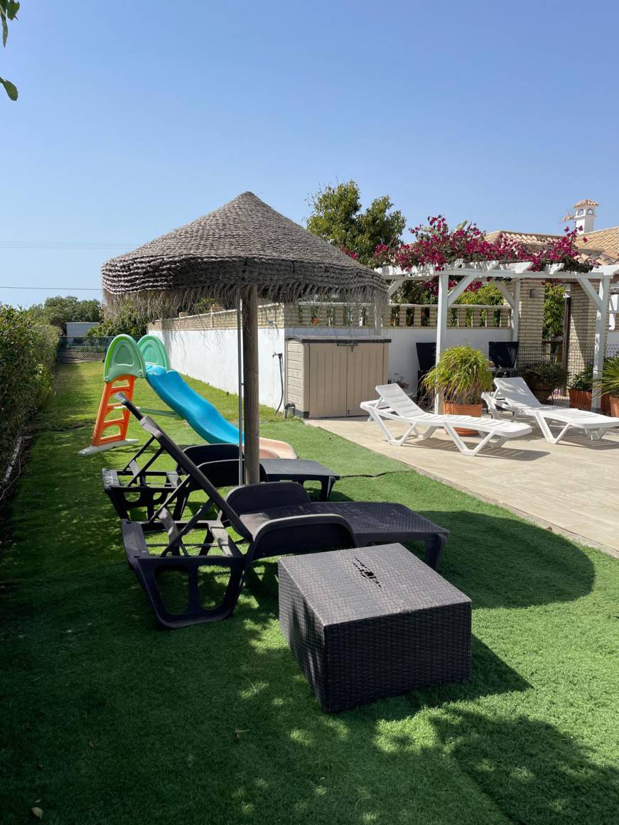 Zona de jardín con tumbonas sombrilla y tobogán junto a terraza de la vivienda