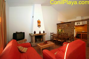 Salón con chimenea, sofás rojos y comedor junto a cocina rústica