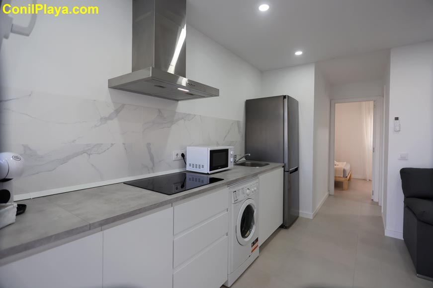 Cocina moderna con lavadora, microondas y frigorífico junto a pasillo