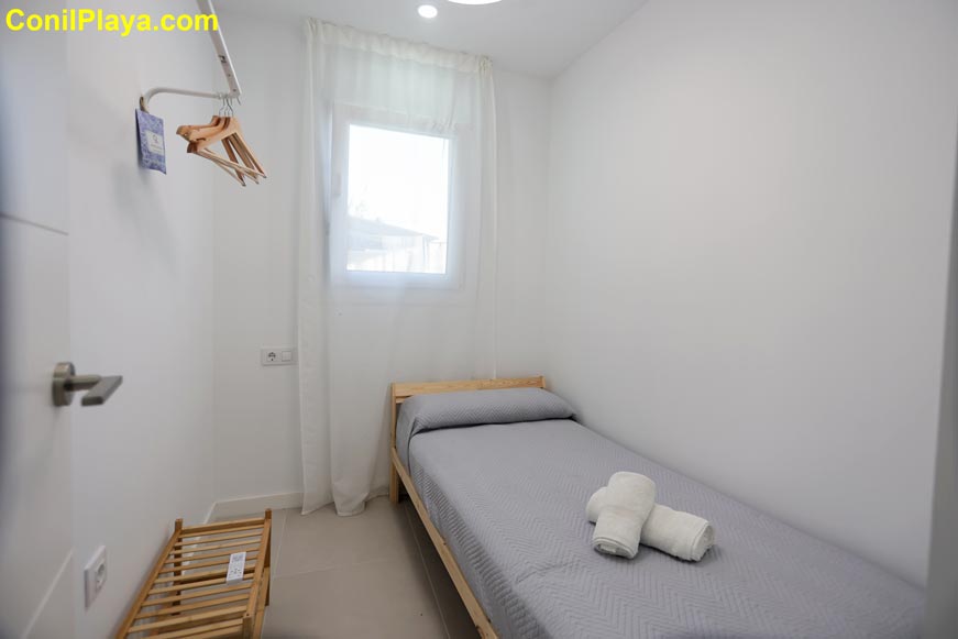 Perspectiva del ormitorio pequeño con cama individual, ventana y paredes blancas
