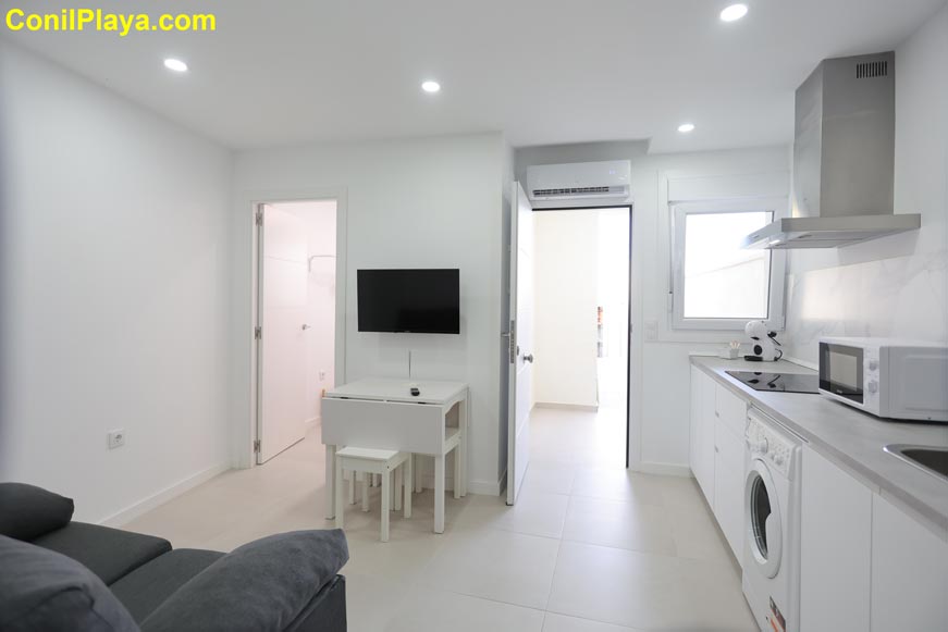 Cocina moderna abierta con lavadora, mesa y televisión vista desde el salón